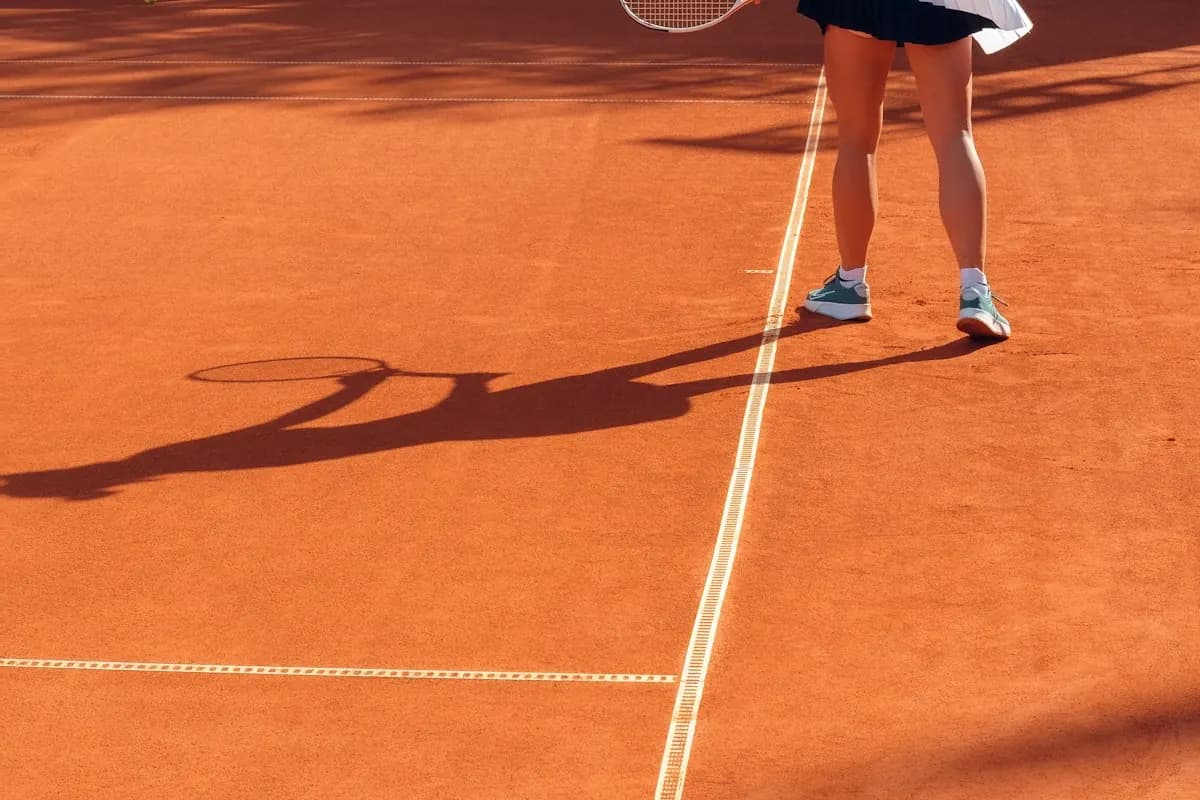 A tennis player on a clay court with a long shadow