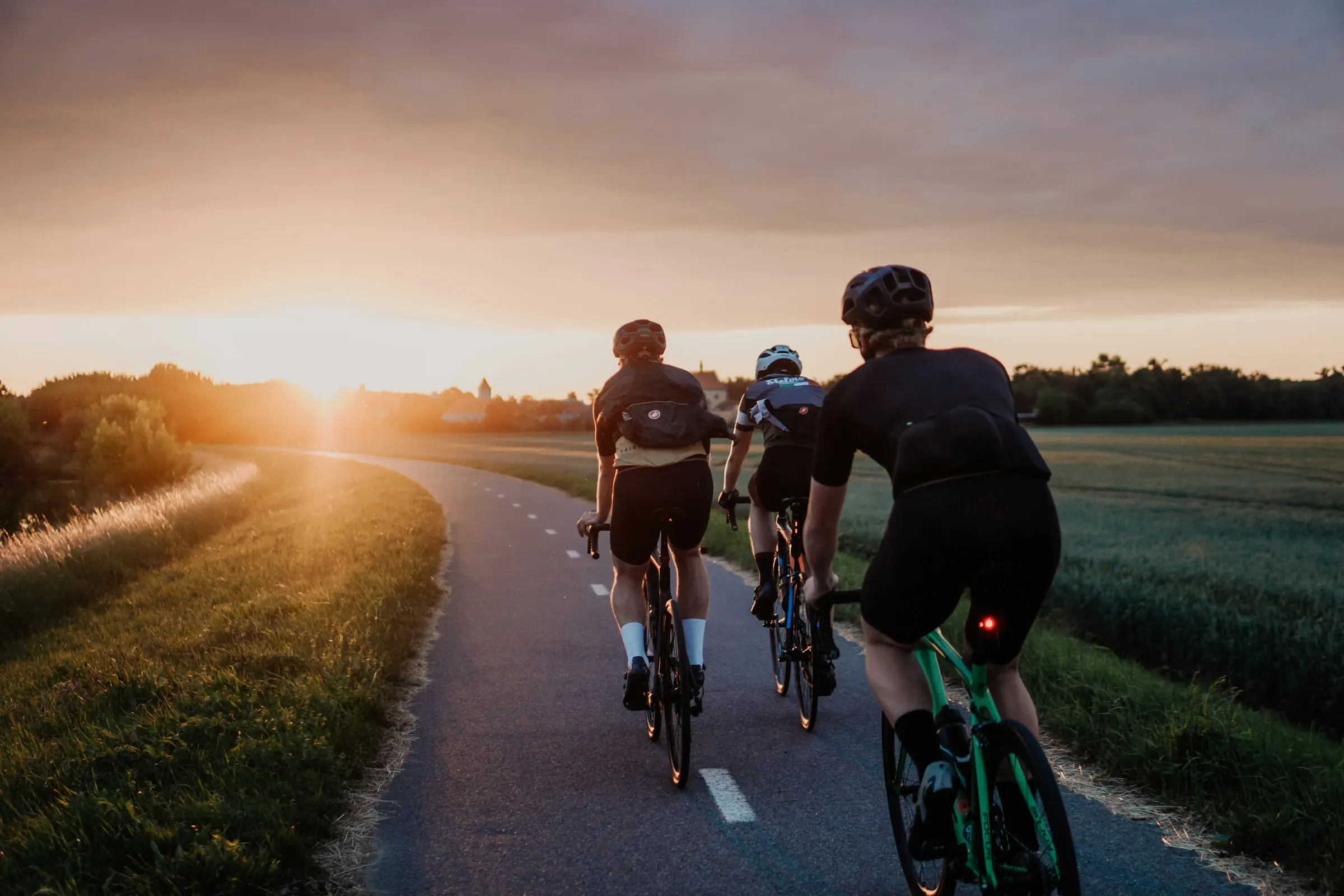 Three cyclists riding a quiet road into the sunset