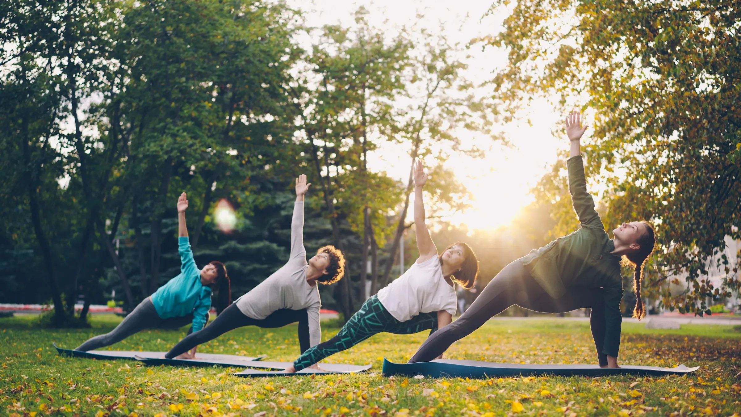 Four people holding a side-angle yoga pose in a sunny park